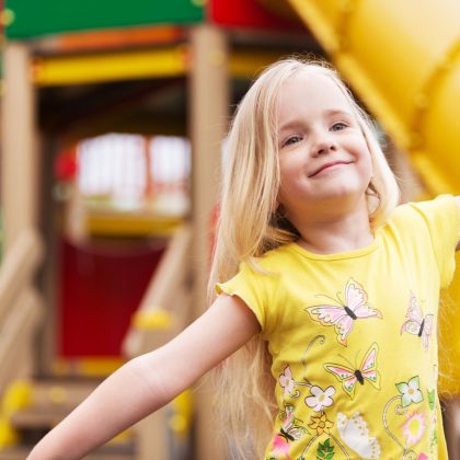 Blonde girl smiling with her arms out at a playground
