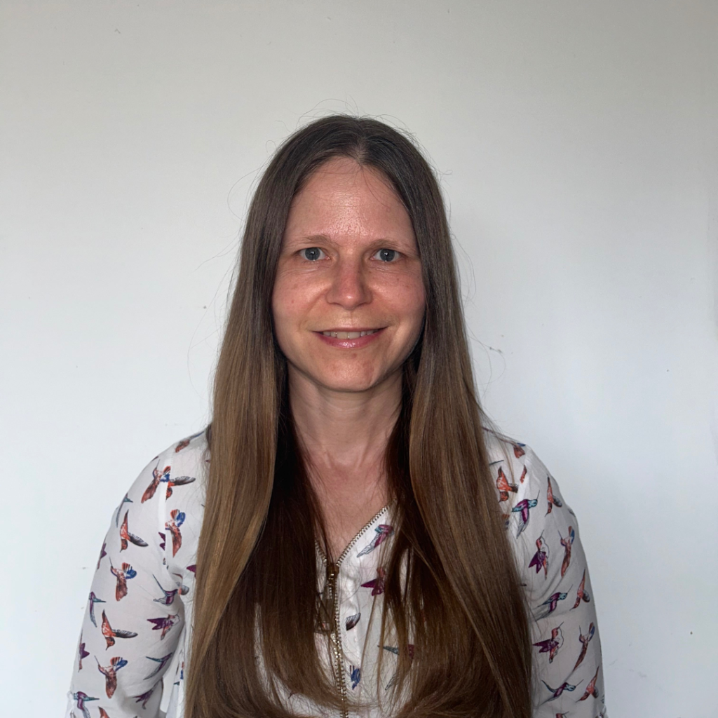Dr Melody Wheaton smiles at the camera. She has long dark hair and is wearing a white patterned top