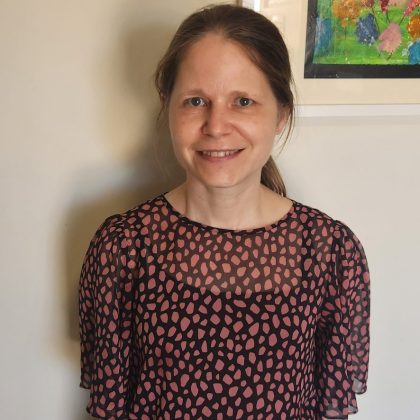 Dr Melody Wheaton smiles at the camera. She had brown hair in a ponytail and is wearing a red spotted blouse.